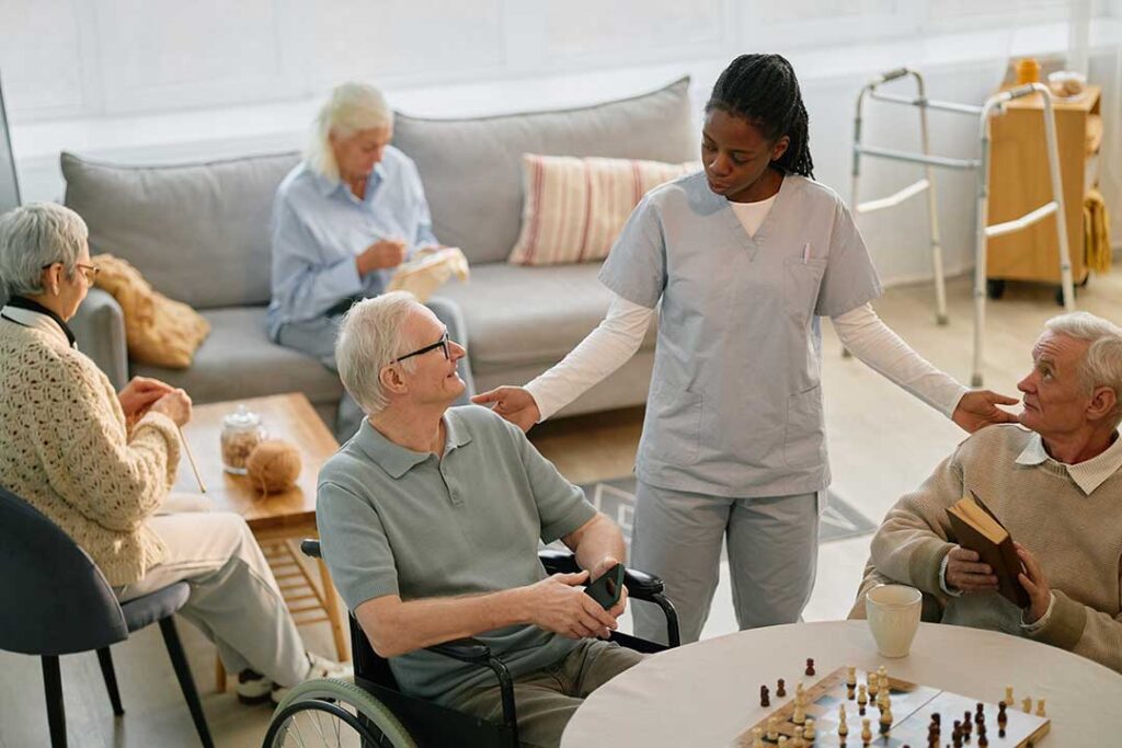 Caregiver speaks respectfully with an older resident in a bright assisted living common area.