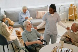 Caregiver speaks respectfully with an older resident in a bright assisted living common area.